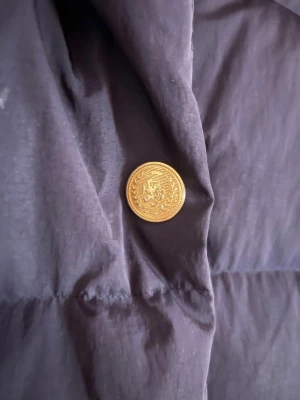 Mörkblå vinterjacka Tommy Hilfiger XS-S - Mörkblå svinsnygg vinterjacka från Tommy Hilfiger med guldiga knappar och broderad logga på ärmen. Jackan har hög krage, dragkedja och knappar framtill. Oversized passform som ger en cool och avslappnad vibe. Perfekt för kalla dagar. Nästan oanvänt och säljs för att det inte var min stil, absolut inget fel på den alls!