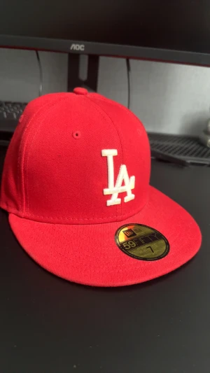 Röd LA Dodgers keps från New Era - Röd 59FIFTY keps från New Era med LA Dodgers logga i vitt framtill. Klassisk flat brim och broderade ventilationshål. Materialet är bomull och insidan har svarta band med 59FIFTY-tryck. Perfekt för dig som gillar streetwear och sport. Kontakta gärna för funderingar🤩