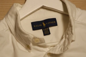 Vit skjorta från Ralph Lauren M - Vit skjorta från Ralph Lauren i klassisk modell med button-down krage och broderad logga på bröstet. Skjortan har långa ärmar, knappar framtill och är gjord i mjuk bomull. Perfekt för dig som gillar stilrena och tidlösa plagg.
