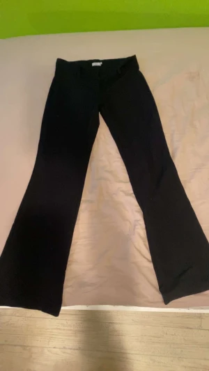 Svarta bootcut kostymbyxor från Nelly - Säljer ett par svarta bootcut byxor från Nelly i storlek 34. Byxorna har låg midja och sitter snyggt över höfterna innan de blir vidare nedtill. Materialet är mjukt och stretchigt, vilket gör dem riktigt sköna att ha på sig. Perfekta för dig som gillar trendiga silhuetter.