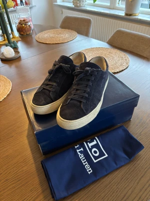 Polo Ralph Lauren skor - Säljer ett par stilrena mörkblå sneakers från Polo Ralph Lauren i mjuk mocka. Skorna har klassisk snörning, vit platt sula och rund tå. Perfekta för dig som vill ha en clean och tidlös look med premiumkänsla.