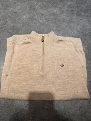 Beige merinoulltröja Morris John half zip - Snygg beige stickad tröja från Morris i 100% merinoull. Modellen har half zip med läderdetalj på dragkedjan och en broderad logga på bröstet. Storlek S, skulle säga att den sitter som en S/XS. Bara använd fåtal gånger, för liten för mig då jag är en M. Väldigt fint skick! Nypris 1899 kr.