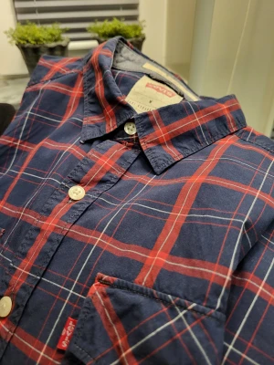 Rutig skjorta från Levi's i marinblått - Säljer en klassisk rutig skjorta från Levi's i marinblått och rött. Skjortan har två bröstfickor med lock, vita knappar och en snygg krage. Perfekt för dig som gillar en avslappnad men ändå stilren look.