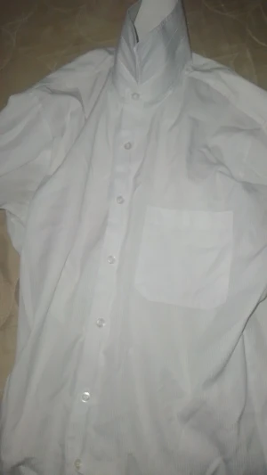 Vit skjorta från Maria med ficka - Klassisk vit skjorta från Maria med diskreta ränder, bröstficka och knappar framtill. Skjortan har lång ärm och rak passform, perfekt för en clean och stilren look. Materialet känns lätt och andas bra.