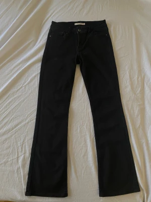 Svarta Levi's 715 Bootcut jeans - Svarta jeans från Levi's i modellen 715 Bootcut. Snygg bootcut-passform med klassiska fem fickor och knappstängning fram. Jeansen är tillverkade i stretchigt denim som sitter skönt och har en stilren look. Perfekta för dig som gillar en tidlös och cool stil.