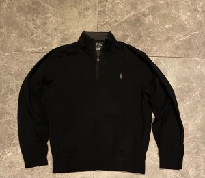 Polo Ralph Lauren Half-Zip – Storlek XS - Säljer en klassisk svart half-zip från Polo Ralph Lauren i mycket bra skick. Tröjan är sparsamt använd och har inga skador, fläckar eller noppor. Loggan är intakt och passformen är snygg och stilren. Så hör gärna av dig eller skriv om du har några frågor!!