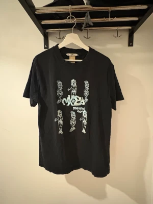 Svart t-shirt med tryck från Eytys - Svart t-shirt från Eytys i storlek XL med coolt grafiskt tryck på framsidan som föreställer tecknade figurer och text. Klassisk rund hals och korta ärmar. Tillverkad i mjuk bomull, perfekt för dig som gillar streetwear och unik design. Nypris: 800kr