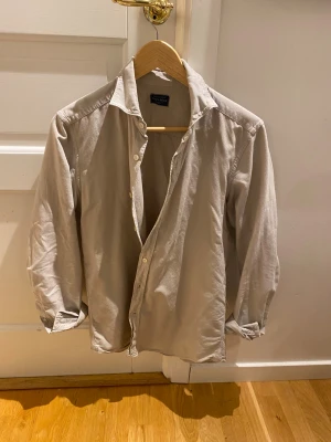 Beige skjorta från Rose & Born - Stilren beige skjorta från Rose & Born med klassisk krage och knäppning framtill. Skjortan är i ett mjukt linnematerial och har långa ärmar. Perfekt för dig som gillar en clean och enkel look. Bra skick