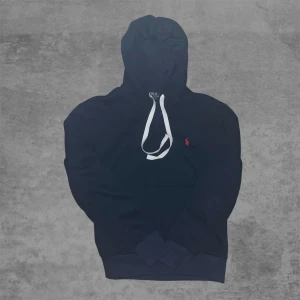 Marinblå hoodie från Polo Ralph Lauren - Snygg och bekväm mörkblå hoodie i mjukt material. Hoodien har justerbara vita dragsnören och en diskret broderad logga i rött på bröstet. Perfekt för vardagsbruk, streetwear-stil eller mysiga dagar hemma. Känguruficka framtill och ribbade muddar för en bra passform.  Skick: Bra begagnat skick Färg: Mörkblå Detaljer: Broderad röd logga, vita dragsnören, känguruficka     #hoodie #sweatshirt #streetwear #blåhoodie #casualstyle #vardagsstil #unisexfashion #bekväm #logohoodie #trendigt