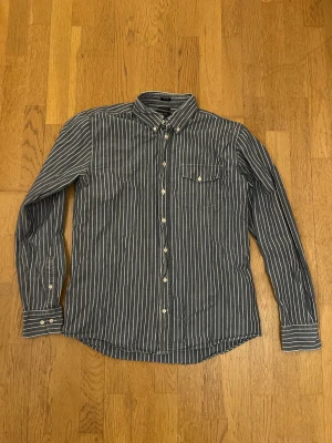 Blåvit randig skjorta från Boomerang - Snygg blå skjorta med vita ränder från Boomerang, tillverkad i 100% ekologisk bomull. Skjortan har klassisk krage, knappstängning hela vägen och en bröstficka med knapp. Passformen är normal och den har långa ärmar med manschettknappar.