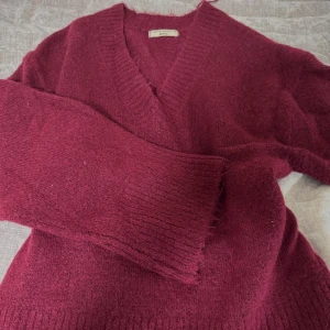 Vinröd stickad kofta från Gina Tricot - Mysig vinröd stickad kofta från Gina Tricot med djup v-ringning och breda ribbade muddar. Perfekt för lager-på-lager och chill dagar. Snygg och enkel att matcha med jeans eller kjol.