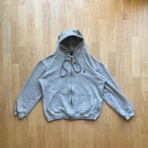 Ralph Lauren Grå Zip-Hoodie (L, kan vara dam/barnstorlek)  - Grå Ralph lauren zip hoodie I mycket fint skick. Mjuk och bekväm, perfekt för en avslappnad och tidlös stil ‼️ Kan vara damstorlek eller barnstorlek (märkt L) - se mått för bästa passformen innan du köper  ‼️ Mått tagna på platt mark: Längd - 58cm Axelbredd - 49 cm Ärm - 51 cm Bröstvidd - 55 cm 