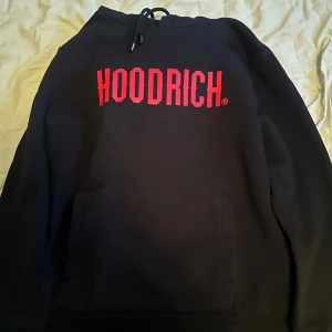 Svart HOODRICH hoodie med röd logga - Svart hoodie från HOODRICH med stor röd logga på bröstet. Nästintill helt ny och oanvänd.