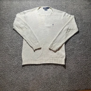 stickad tröja från Polo Ralph Lauren - Vit stickad tröja från Polo Ralph Lauren i 100% bomull. Klassisk modell med rund halsringning, ribbade muddar och liten broderad logga på bröstet. Perfekt för lager-på-lager och chill stil.