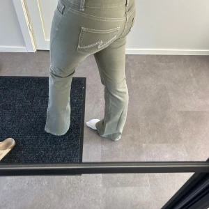 Bootcut byxor från Nelly - Snygga gröna bootcut-byxor från Nelly med låg midja och vita kontrastsömmar. Storlek 38 och bra skick.