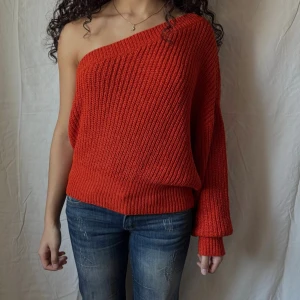 Röd stickad oneshoulder-tröja - Röd stickad tröja med oneshoulder-design. Tröjan har en lös passform, bred ribbad kant och långa ärmar. Perfekt nu till hösten för dig som vill sticka ut med en cool och trendig look.