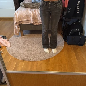 Mörkgrå bootcut jeans med låg midja - Snygga mörkgrå jeans med bootcut och låg midja. Klassisk femficksmodell med silverfärgade knappar och dragkedja. Jeansen har en lätt tvättad look och är tillverkade i mjukt denimtyg som sitter skönt. 