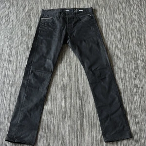 Replay Waitom svarta jeans, storlek 33 - Svarta jeans från Replay, modell Waitom, med klassisk femficksdesign och raka ben. Jeansen har snygga detaljer vid fickorna och är tillverkade i slitstarkt jeansmaterial med en stilren look som passar till många olika outfits.