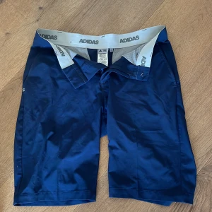 Blå golfshorts från Adidas  - Snygga marinblå golfshorts från Adidas. Klassisk rak passform och tillverkade i ett lätt syntetmaterial perfekt för golf. 