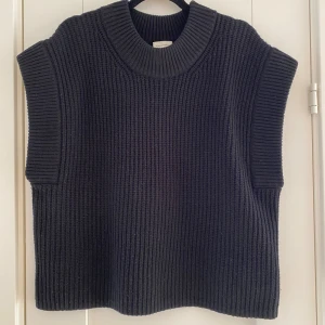 Svart stickad väst By Malene Birger - Säljer en svart, grovstickad väst från By Malene Birger med bred ribbad krage och ärmkanter. Modellen är loose fit och har en rak, boxig siluett som ger en chill vibe. Perfekt att slänga över en t-shirt eller skjorta för en cool layering-effekt.          Mått  Över bröstet: ca 60 cm  Längd från axeln och ner: ca 64 cm   100% ull   Kommer från ett djur och rökfritt hem.  