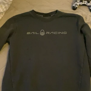 Svart Sail Racing sweatshirt M - Svart sweatshirt från Sail Racing i storlek M. Tröjan har rund halsringning och tryckt logga framtill i grått. Klassisk och stilren modell med långa ärmar, perfekt för en chill och sportig look.