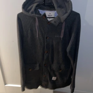 Mörkgrå hoodie-kofta från Wemoto - Säljer en mörkgrå hoodie med knappar från Wemoto i storlek M. Hör av dig vid funderingar!