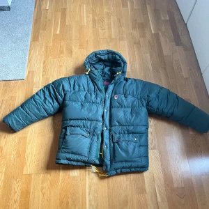 Mörkgrön dunjacka från Fjällräven  - Säljer en mörkgrön dunjacka från Fjällräven i storlek M. Jackan har huva med gula snören, stora fickor med dragkedja och tryckknappar framtill med en oversized fit. Några småhål men som knappt syns💕 säljer då felköp. Buda gärna ❤️rätt stor i storlek 