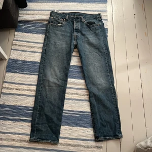 Levi's 501 jeans blå W32 L30 - Klassiska Levi's 501 jeans i blå denim med raka ben och normal passform. Byxorna har fem fickor, knappgylf och den ikoniska läderpatchen bak. Perfekt för dig som gillar tidlös stil och vill ha ett par schyssta jeans i garderoben.