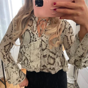 Ormskinnsmönstrad blus från Zara - Slutsåld populär blus i mesh från Zara med ormskinnsmönster i beige och brunt. Blusen har långa, vida ärmar med volang och knyt vid ärmslut samt knytning vid halsen. Materialet är lätt och luftigt. Använd en gång.