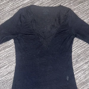 Svart långärmad topp med spets - Svart långärmad topp med djup v-ringning och dekorativ spets runt halsen. Tunn och mjuk, perfekt för att styla med jeans eller kjol. Snygg passform som framhäver siluetten och ger en elegant touch till din outfit.