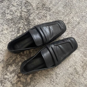 Svarta loafers från Mango i skinn - Stilrena svarta loafers från Mango med klassisk design och fyrkantig tå. Skorna är tillverkade i mjukt skinn och har en platt sula. Använda en gång.