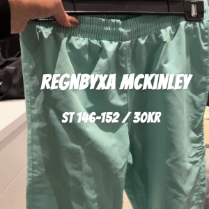 Turkosa regnbyxor från McKinley - Turkosa regnbyxor från McKinley med elastisk midja och raka ben. Perfekta för blöta dagar och utomhusaktiviteter. Lätta att dra på över andra kläder och håller dig torr när det regnar.