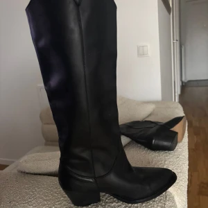 Sofie Schnoor svarta höga boots i skinn - Säljer ett par svarta boots med hög skaft och spetsig tå i äkta skinn. Snygg, stilren design med låg klack och platt sula. Perfekta för dig som gillar klassiska och tidlösa skor med lite edge. Passar till både jeans och kjol.