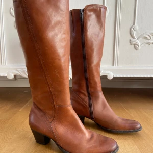 Bruna skinnstövlar Tamaris - Snygga bruna stövlar från Tamaris i äkta skinn med medelhög klack och rund tå. Stövlarna har dragkedja på insidan för enkel på- och avtagning. Perfekt till höstens och vinterns outfits för en stilren look. Använda fåtal gånger och är jättefina! Och sköna! 