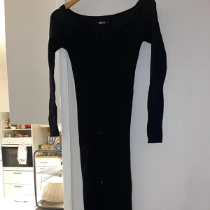 Svart ribbad långklänning Gina Tricot - Svart långklänning från Gina Tricot med ribbad struktur och v-ringning. Klänningen har lång ärm och är figurnära i modellen, perfekt för dig som gillar en stilren och enkel look. Materialet är stickat och stretchigt för en bekväm passform.