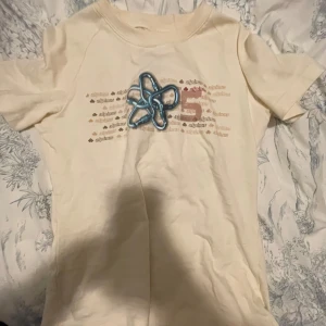 Beige t-shirt från Alpinus XS - Säljer en beige t-shirt från Alpinus i storlek XS, limited edition. T-shirten har korta ärmar och är gjord i mjuk bomull. Framsidan har ett tryck med Alpinus-logga och grafiska detaljer i olika färger samt en blå 3D-dekoration. Perfekt för dig som gillar unika plagg.