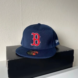 boston red sox new era - Snygg marinblå Boston Red Sox keps från New Era 59FIFTY med röd och vit broderad B-logga framtill och MLB-logga bak. Klassisk flat brim och stilren design. Materialet är 70% akryl och 30% ull. Perfekt för dig som gillar baseball eller streetwear.