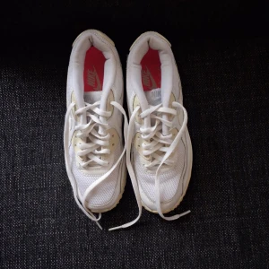 Nike Air Max 90 vita sneakers - Säljer ett par klassiska Nike Air Max 90 sneakers i helvitt med mesh och skinnpaneler. Skorna har den ikoniska synliga Air-sulan, rund tå och snörning. Perfekta för dig som gillar en clean och sportig look. Röd innersula med Nike-logga.