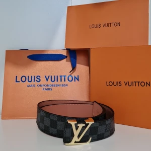 L&V utigt skärp med L&V-spänne - Snyggt L&V-bälte i svart och grått rutigt mönster med ikoniskt L&V-spänne i guld. Bältet är gjort i exklusivt skinn och har en klassisk, stilren design som passar perfekt till jeans eller kostymbyxor.