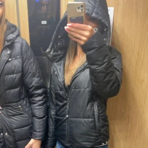 Svart pufferjacka från Nike - Säljer en svart pufferjacka från Nike med vit logga på bröstet. Jackan har huva, dragkedja framtill och en snygg, lite oversized passform. Perfekt för kalla dagar och enkel att matcha med olika outfits.