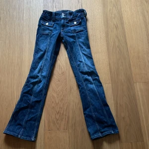 Blå bootcut jeans från H&M, stl 158 - Snygga blå bootcut jeans från H&M i storlek 158. Jeansen har låg midja, justerbar midja och coola fickor med knappar framtill. Perfekt för dig som gillar en klassisk men trendig look. Materialet är jeans och färgen är mörkblå.
