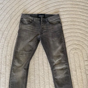 Grå jeans från Chasin’ i slim fit - Säljer ett par grå jeans från Chasin’ med snyggt tvättad look och klassiska fem fickor. Jeansen har slim fit-passform och raka ben, samt coola detaljer på bakfickorna. Perfekta till en avslappnad streetstil.