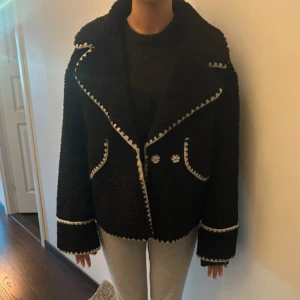 Svart teddyjacka från Object - Säljer en snygg svart teddyjacka från Object med vita detaljer. Jackan har långa ärmar och knappar framtill. Perfekt för att hålla sig varm och stilren under kyliga dagar.