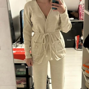 Beiga set med knyt och fickor - Säljer ett set ”mjukis”i mjukt material med matchande knytband i midjan. Byxorna har raka ben och är dekorerade med snygga fickor framtill med flätad kant och pärlknapp. Perfekta för en chill och avslappnad look. Oanvänd