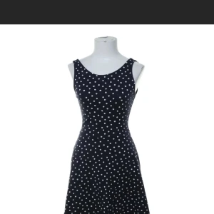 Marinblå prickig ärmlös klänning strl 36 - Snygg marinblå klänning med vita prickar och ärmlös design. Klänningen har rundad halsringning fram och djupare rygg, vilket ger en cool och feminin siluett. Passformen är normal och tyget känns mjukt och följsamt, perfekt för dig som gillar retrovibbar och stilren look.