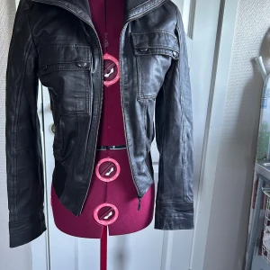 Mörkbrun skinnjacka från Mexx, stl 36 - Mörkbrun mjuk skinnjacka från Mexx i klassisk pilotstuk. Jackan har dragkedja framtill, två bröstfickor med lock och långa ärmar. Materialet är äkta skinn och jackan har ribbade detaljer vid krage och midja.