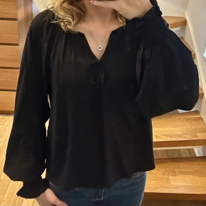 Svart blus med knyt från Lindex - Svart blus från Lindex i storlek S. Modellen har långa ärmar, lös passform och snygg knytning vid halsen. Tunt och mjukt material som faller snyggt. Perfekt till höst/vinter!!