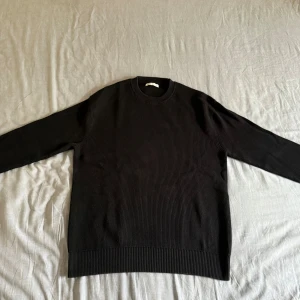 Ribbad Zara Tröja - Svart stickad tröja med ribbad struktur och rund hals. Tröjan har långärmade ärmar och breda muddar vid ärmslut och nederkant. Enkel och clean design som funkar till många olika stilar. Perfekt för dig som gillar minimalistiskt och stilrent.