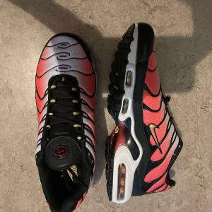 Nike Air Max Plus TN rosa och svarta - Nike Air Max Plus TN sneakers i en snygg färgskiftning från rosa till vitt med svarta vågformade detaljer och guldiga swoosh. Skorna har synlig Air Max-dämpning, svart sula och snörning. Perfekta för dig som vill sticka ut med en unik och sportig look.
