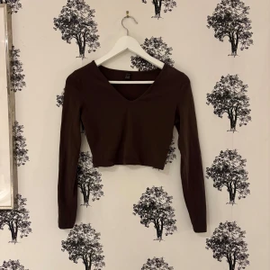 Brun croppad långärmad topp Shein - Mörkbrun croppad topp från Shein med lång ärm och v-ringad hals. Enkel och stilren design i mjuk bomullskänsla, perfekt att matcha med jeans eller kjol. Sitter tight och har en snygg passform som framhäver midjan.